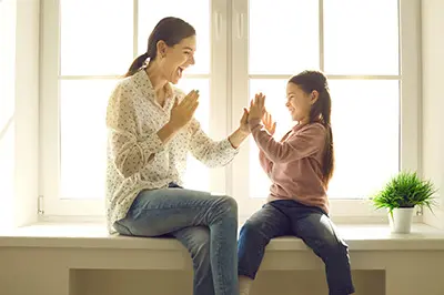 Mama z córką grają w łapki przy oknie