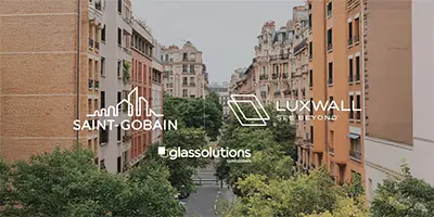 na tle zielonego osiedla logotypy Saint-Gobain Glass, LUXWALL i Glassolutions